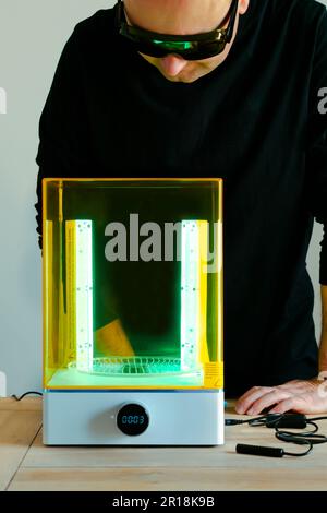 Mann mit Brille, der vor Gebrauch eine Wasch- und Heilungsmaschine mit UV-Licht justiert, für 3D-Harzdrucker Stockfoto