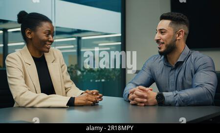 Arabisch-indischer Geschäftsmann und afroamerikanische Geschäftsfrau, die sich im Büro unterhielten, erörterten die Geschäftsidee eines Projekts am Tisch. Vielfältige Partner Stockfoto