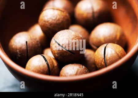 Makroaufnahme von getrockneten organischen Macadamianüssen in orangefarbener Keramikschüssel Stockfoto