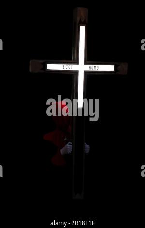 Ein Mitglied des Hermandad del Santo Cristo de los Artilleros trägt während einer Semana Santa Prozession in Valladolid, Spanien, ein beleuchtetes Kreuz Stockfoto