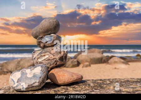 Steinpyramiden und Glaskugel am traumhaften Ostsee-Sandstrand auf Rügen zum spektakulären orange Sonnenuntergang Stockfoto