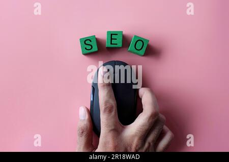 Hand-Klick-Computermaus mit Text SEO auf pinkfarbenem Hintergrund. Konzept der Suchmaschinenoptimierung. Stockfoto
