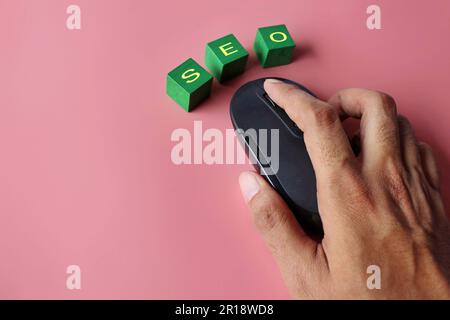 Hand-Klick-Computermaus mit Text SEO auf pinkfarbenem Hintergrund. Konzept der Suchmaschinenoptimierung. Stockfoto