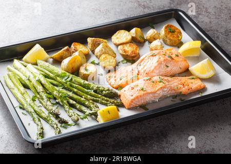 Diätessen Lachsfilet gebacken mit Spargel und neuen Kartoffeln Nahaufnahme auf einem Backblech auf dem Tisch. Horizontal Stockfoto