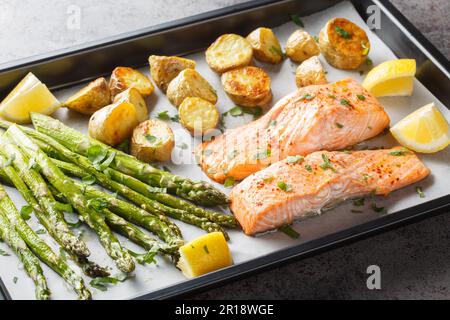 Frisch gebackenes Lachsfilet mit Spargel und Kartoffeln in Nahaufnahme auf einem Backblech auf dem Tisch. Horizontal Stockfoto
