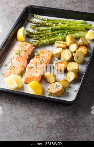 Gebackenes würziges Lachsfilet mit Spargel und Kartoffeln in Nahaufnahme auf einem Backblech auf dem Tisch. Vertikal Stockfoto