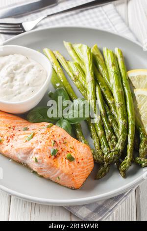 Gebackenes Lachsfilet mit Spargel, serviert mit Tartar-Sauce, Nahaufnahme auf einem Teller auf dem Tisch. Vertikal Stockfoto