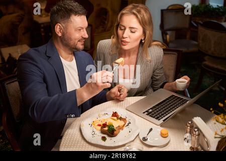 Verspielter Mann, der seine Freundin mit leckerem Mittagessen füttert, flirtet Stockfoto