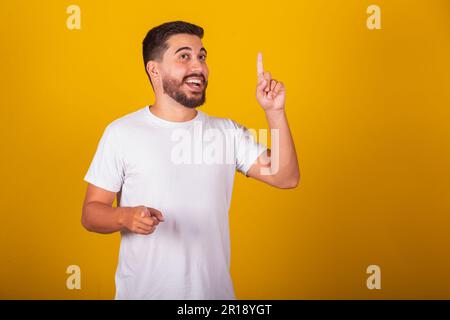 Brasilianischer Lateinamerikaner, mit erhobenen Fingern für Idee, Antwort, entdeckt, weiß, gelöst. Konzept von Idee, Schöpfung. Gelber Hintergrund Stockfoto