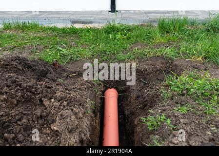 Orangefarbenes PVC-Rohr, das im Boden vergraben ist und mit der Dachrinne verbunden ist, wird zur Verbindung mit der Ablaufleitung verwendet. Stockfoto