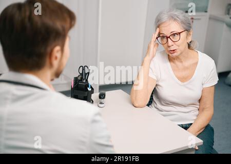 Ältere Dame beschwert sich beim Arzt über Kopfschmerzen Stockfoto