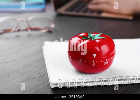 Frau, die am Laptop am Holztisch arbeitet, konzentriert sich auf die Küchenuhr in Form von Tomaten. Platz für Text Stockfoto