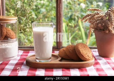 Glas Milch mit Keksen auf roter karierter Tischdecke im Innenbereich Stockfoto