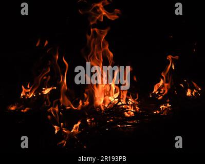 Flamme mit brennenden roten, heißen Funken auf schwarzem Hintergrund. Die Flamme und der schwarze Hintergrund schaffen interessante Strukturen Stockfoto