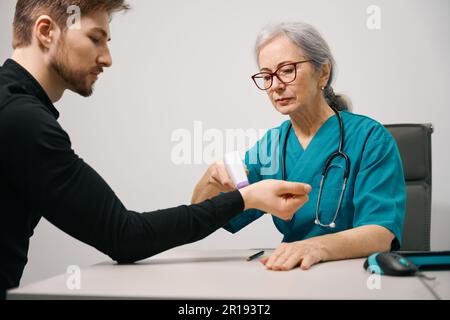 Junger bärtiger Mann, weibliche Ärztin misst die Temperatur mit einem modernen Thermometer Stockfoto