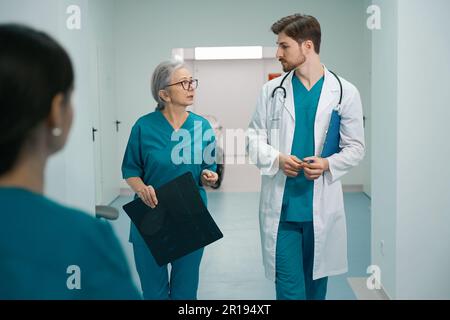 Junger Mann und ältere Frau gehen, reden entlang des Krankenhauskorridors Stockfoto