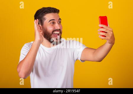 Brasilianischer Lateinamerikaner, Selfie mit Handy, Videoanruf, Gespräch, Lächeln, Fotografieren. Gelber Hintergrund. Stockfoto