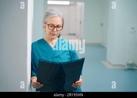 Ältere Frau Sanitäterin steht im Krankenhauskorridor mit MRT-Scan Stockfoto