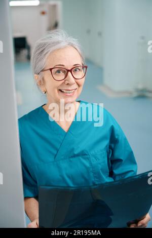 Lächelnde Sanitäterin steht im Krankenhauskorridor mit mrt-Scan Stockfoto