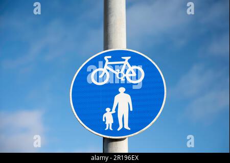 Blauweißes Kreisschild in Großbritannien für Radfahrer und Fußgänger. Auf Metallpfosten, isoliert gegen natürlichen blauen Himmel und Wolkenhintergrund. Sonniger Tag. Stockfoto