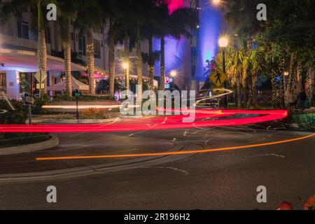 Sarasota, FL, USA – 10. April 2023: Farbenfrohe Kreuzung bei Nacht im Unterhaltungsviertel der Innenstadt mit roten Lichtpfaden. Stockfoto