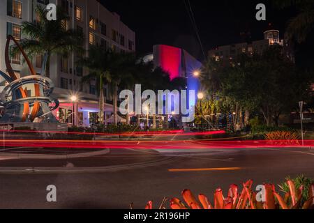 Sarasota, FL, USA – 10. April 2023: Farbenfrohe Kreuzung bei Nacht im Unterhaltungsviertel der Innenstadt mit roten Lichtpfaden. Stockfoto