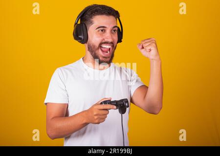 Ein glücklicher brasilianischer Mann aus Lateinamerika mit Headset und Videospielcontroller spielt und feiert, wer gewonnen hat Stockfoto