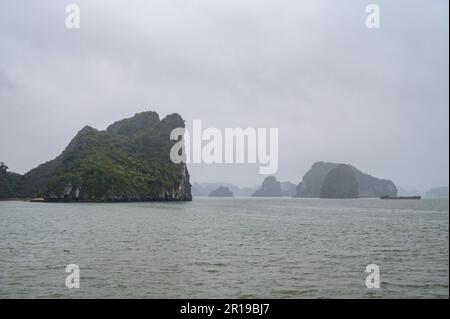 Die typischen Kalksteininseln und Inseln in niedrigen Wolken und Nebel in der Bai TU Long Bay, Halong Bay, Vietnam. Stockfoto