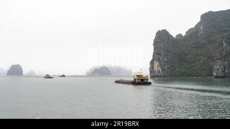 Lastkähne und Boote, die zwischen den charakteristischen Kalksteininseln und Inseln segeln, die in den Nebel in der Bai TU Long-Bucht, Halong-Bucht, Vietnam verblassen. Stockfoto