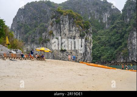 Touristen ruhen sich zwischen Kajakfahrten in der Bai TU Long Bay, Halong Bay, Vietnam an einem feinen Sandstrand aus. Stockfoto
