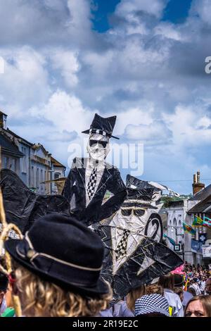 Leute, die große mit- und Papierfiguren von unhöflichen zwei-Ton-Figuren bei der Mazey-Day-Parade beim Golowan Festival in Penzance in Cornwall i dabei hatten Stockfoto