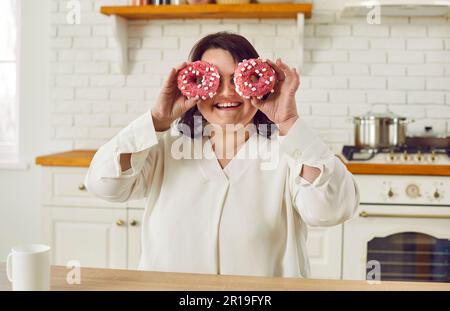 Nahaufnahme eines fröhlichen, lächelnden, dicken, dicken Weibes, das Spaß mit Donut-Kuchen auf den Augen hat. Stockfoto