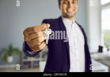 Nahaufnahme eines Hausschlüssels in der Hand eines glücklichen männlichen maklers von der Immobilienagentur. Stockfoto