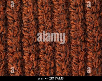 Eine schöne Nahaufnahme eines handgestrickten warmen und weichen Wollmusters. Textur eines braunen Pullovers, Socken oder Halstuchs. Hintergrund aus orangefarbenem Strickmaterial Stockfoto