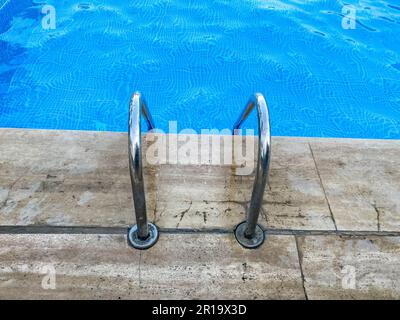 Verchromte Metalltreppe mit Geländer, um in den Pool zu steigen, wo man schwimmen und mit warmem, klarem, blauem Wasser in einem tropischen Hotel baden kann Stockfoto