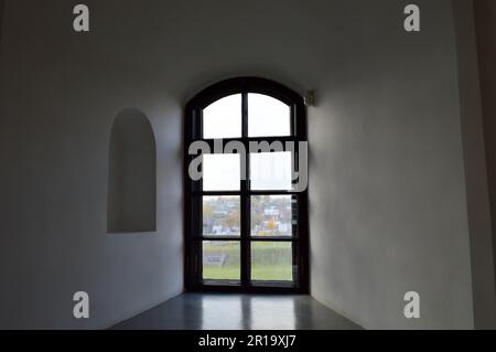 Ein kleines, schmales schwarzes Fenster mit einem Rahmen auf einer alten, alten, steinweißen, dicken Betonwand in einer alten Burg. Der Hintergrund. Stockfoto