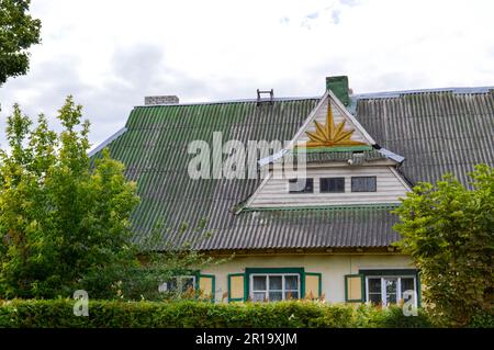 Ein altes rustikales europäisches Holzhaus aus Brettern mit Fenstern und Fensterläden mit einem dreieckigen Dach mit Schiefer, der mit Moos gegen A überwuchert ist Stockfoto