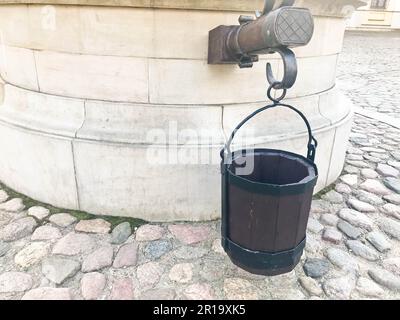 Ein alter, kleiner, alter, antiker Eimer mit Brettern für einen Brunnen vor dem Hintergrund der gepflasterten amenia Straße. Stockfoto