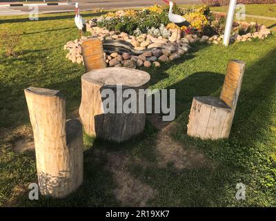 Wunderschöne hausgemachte Holzstühle und ein Tisch aus Holz, Baumstümpfe auf der Straße unter dem offenen Himmel. Hausgemachtes Landschaftsdesign. Stockfoto