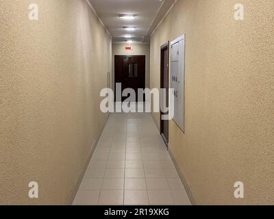 Langer schmaler gelber, beigefarbener Korridor mit Apartments in einem neuen, modernen Gebäude. Stockfoto