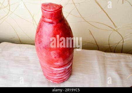 Gefrorene gemahlene Erdbeeren. Gefrorene Beeren in Form einer Flasche auf beigefarbenem Hintergrund. Stockfoto