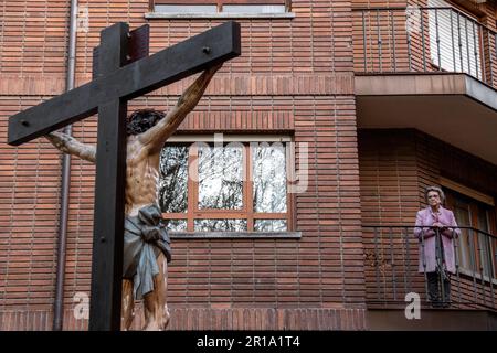 Eine Frau schaut sich einen Paso der Bruderschaft der Strafe der Heiligen Leidenschaft Christi von ihrem Balkon aus an, während Semana Santa in Valladolid, Spanien Stockfoto