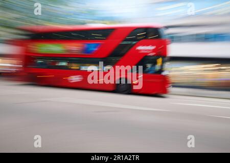 Ein roter Londoner Doppeldeckerbus, der im Stadtzentrum vorbeifährt und eine Langzeitbelichtungstechnik verwendet, um Bewegungsunschärfe zu erzeugen Stockfoto