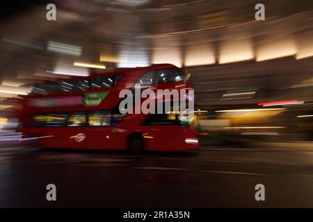 Ein roter Londoner Doppeldeckerbus, der im Stadtzentrum vorbeifährt und eine Langzeitbelichtungstechnik verwendet, um Bewegungsunschärfe zu erzeugen Stockfoto