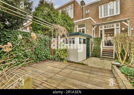 Ein Hinterhofbereich mit einem Schuppen und einigen Pflanzen auf dem Boden vor einem Ziegelhaus, umgeben von Bäumen Stockfoto