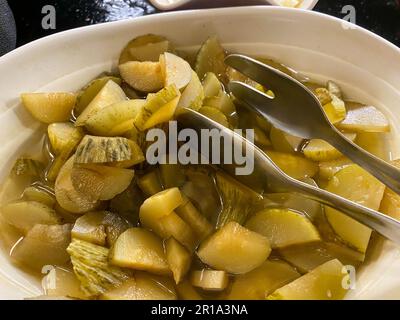 Köstliche grüne, frisch eingelegte Gurken, in kleine Stücke geschnitten, gesunder Gemüsesalat in einem Teller mit Zange geschnitten. Stockfoto