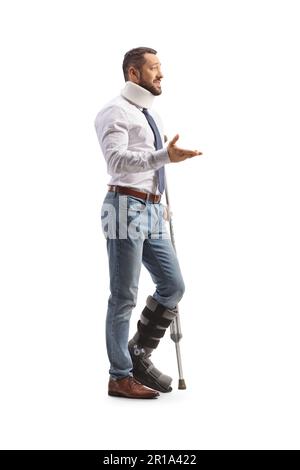 Junger Mann mit orthopädischem Stiefel und Halskragen, der mit Krücke steht und spricht, isoliert auf weißem Hintergrund Stockfoto