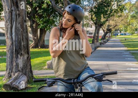 Porträt einer jungen Frau auf ihrem Fahrrad, die einen schwarzen Helm aufsetzt Stockfoto