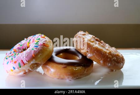 Drei Donuts auf weißem Teller, rosa mit Schokolade und süßem Nachtisch bedeckt mit Pulverhintergrund für Restaurantmenüs Stockfoto