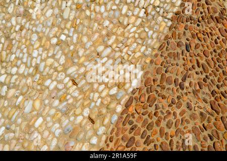 Die Textur der Steinmauer, die Straße aus kleinen runden und ovalen Steinen mit abstrakten Linien, die Muster mit zweifarbigen sandigen Nähten von natürlichem o darstellen Stockfoto